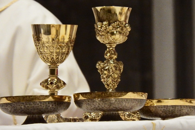 Two gold chalices and three bowls containing communion wafers.
