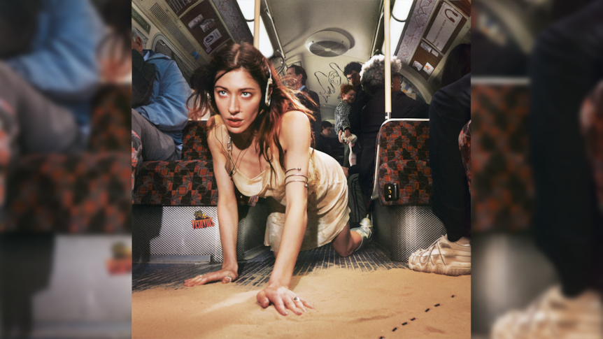 Caroline Polachek on hands and knees on the floor of a train car that is covered in sand
