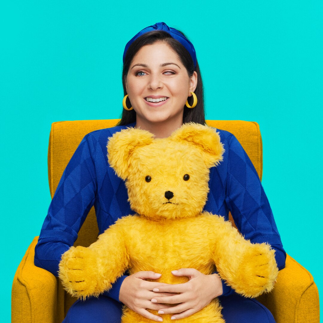 Nas Campanella wearing a blue dress sitting on a yellow chair holding a yellow toy bear from Play School called Big Ted.