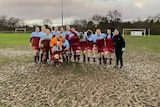 A group of female soccer players standing huddling on a muddy pitch. 