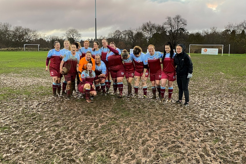 Un groupe de joueuses de football se tenant debout sur un terrain boueux. 