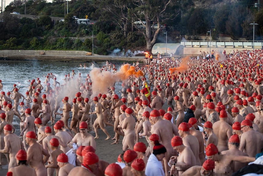 Hundreds of people in red caps but no other cloths run into the water. 