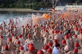 Hundreds of people in red caps but no other cloths run into the water. 