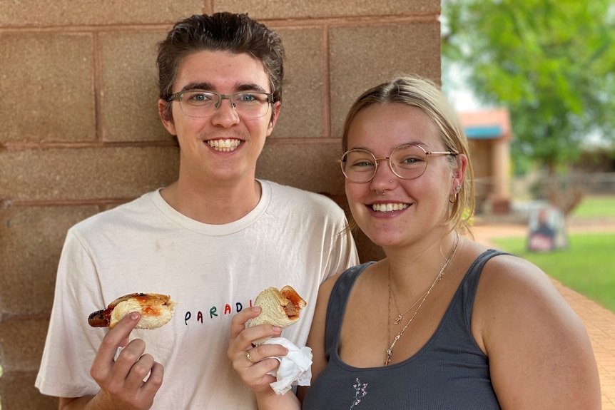 Two young people wearing glasses eat hot dogs