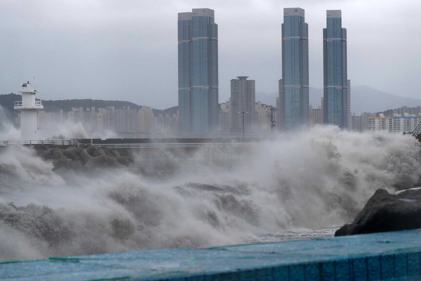 Waves crash onto shore with city buildings in background