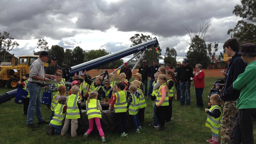 Children gather around a large tractor tyre and listen to local farmers speak about farm safety