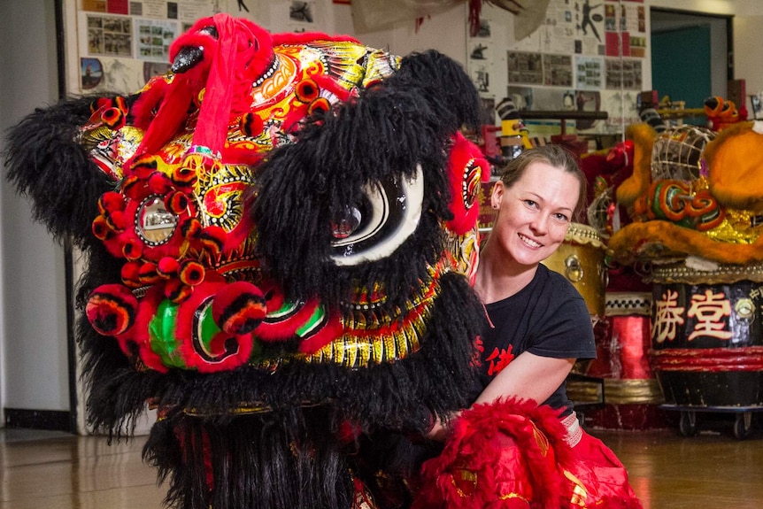 A woman posing with a red and black coloured Chinese lion dance costume head.