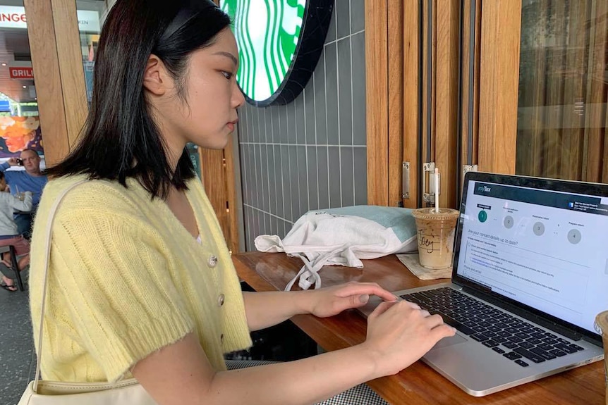 A side-on profile of a young woman of Asian appearance typing on a laptop at a Starbucks Cafe.