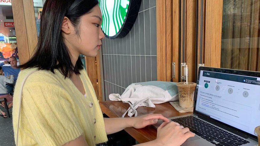 A side-on profile of a young woman of Asian appearance typing on a laptop at a Starbucks Cafe.