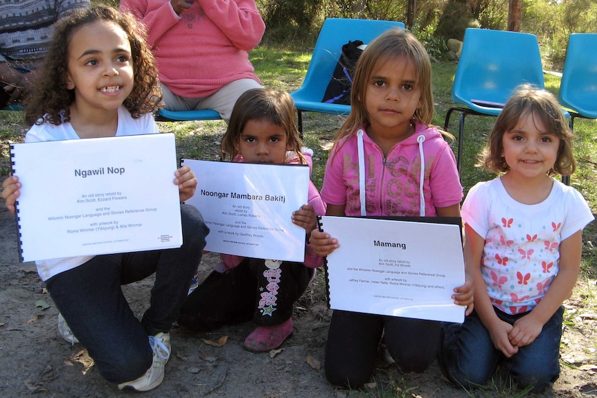 Four girls sit on the ground holding signs.