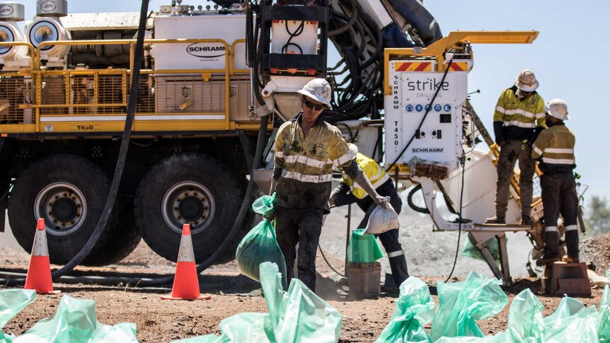 A mining worker wearing high-vis clothing carrying drilling samples.