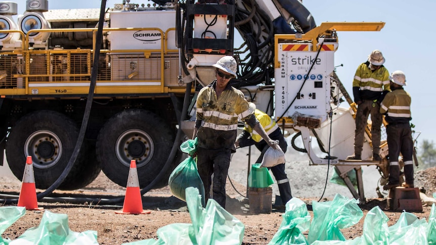 A drill rig offsider carries samples in the outback while searching for gold.