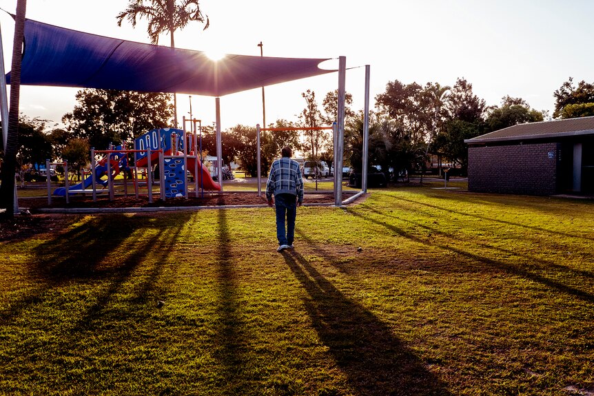 A playground and toilet block at sunset as a man walks with back to camera on grassy land.