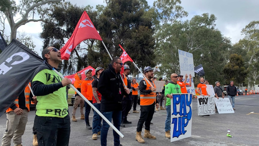 Trade workers holding CFMEU flags and placards that say 'pay up'