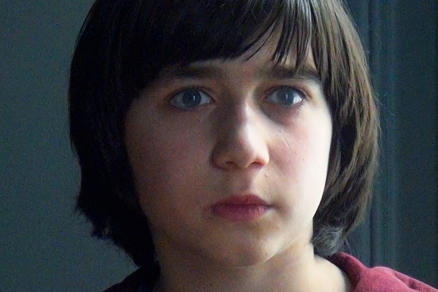 A film still of Milo Machado Graner, a young boy with blue eyes, in close-up.