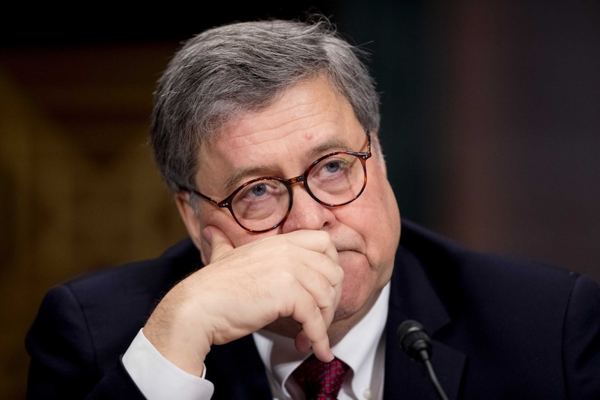 William Barr holds his hand to his mouth as he looks beyond the camera.