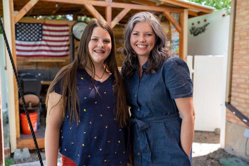 A woman and teen girl stand together in a backyard