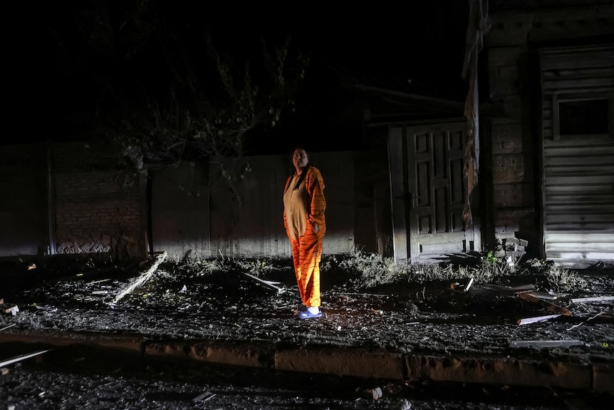 Man stands in his pyjamas around rubble 