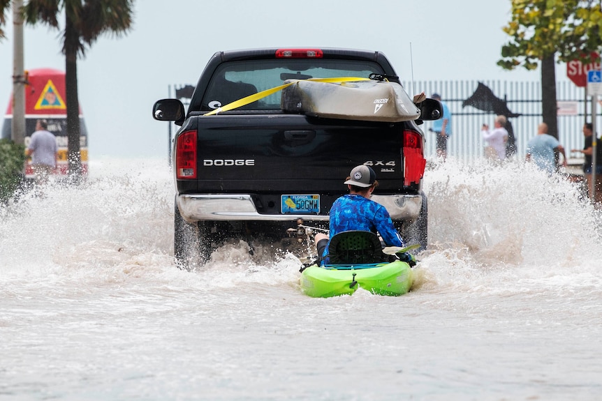 A boy is towed on a floatable ring behind a ute through floodwaters. 