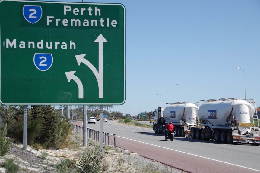 A sign indicates the turnoff to Mandurah and the direction to Perth and Fremantle on Roe Highway, as traffic passes.