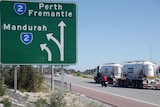 A sign indicates the turnoff to Mandurah and the direction to Perth and Fremantle on Roe Highway, as traffic passes.