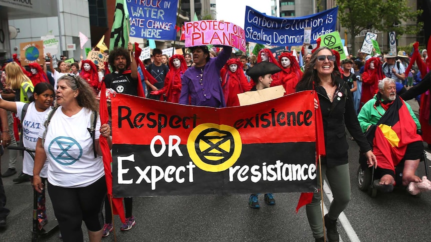 Extinction Rebellion protesters walk behind a big red banner.