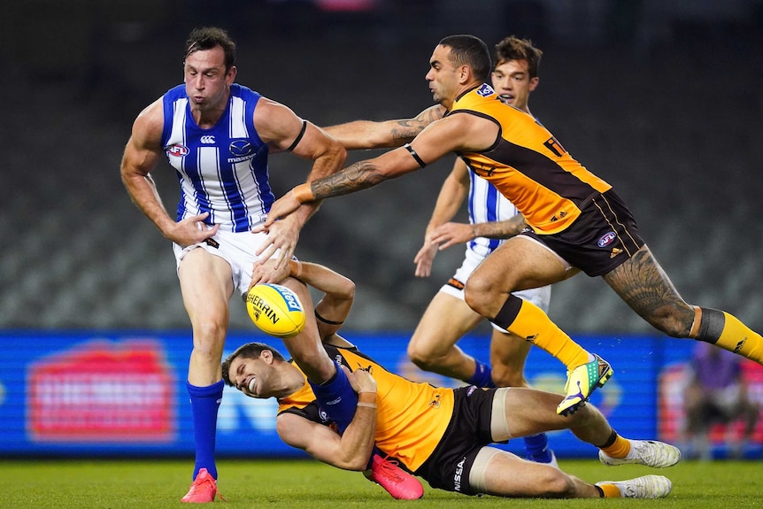 Todd Goldstein stands with his eyes closed and the ball in front of him with a player in yellow singlet holding onto his leg