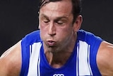 Todd Goldstein stands with his eyes closed and the ball in front of him with a player in yellow singlet holding onto his leg