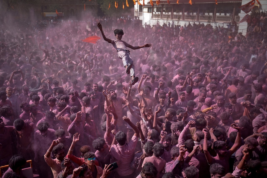 A person is thrown in the air by a crowd of people covered in pink.