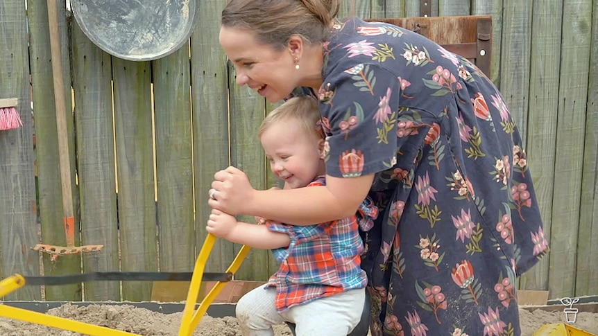 Woman playing with a toddler in a sandpit with an excavator toy.