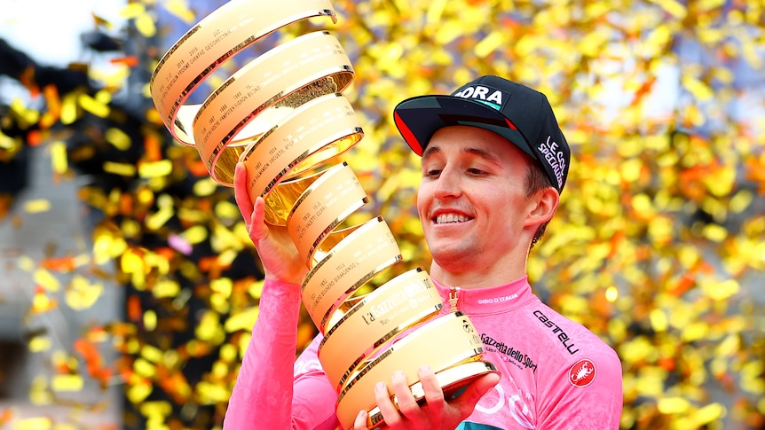 Jai Hindley looks at a golden trophy with gold confetti behind him