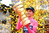 Jai Hindley looks at a golden trophy with gold confetti behind him