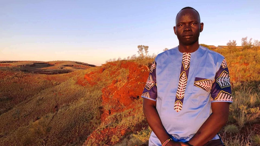 Philip Lako stands looking at the camera, with beautiful golden-hour red dirt hills and scrubland in the background.