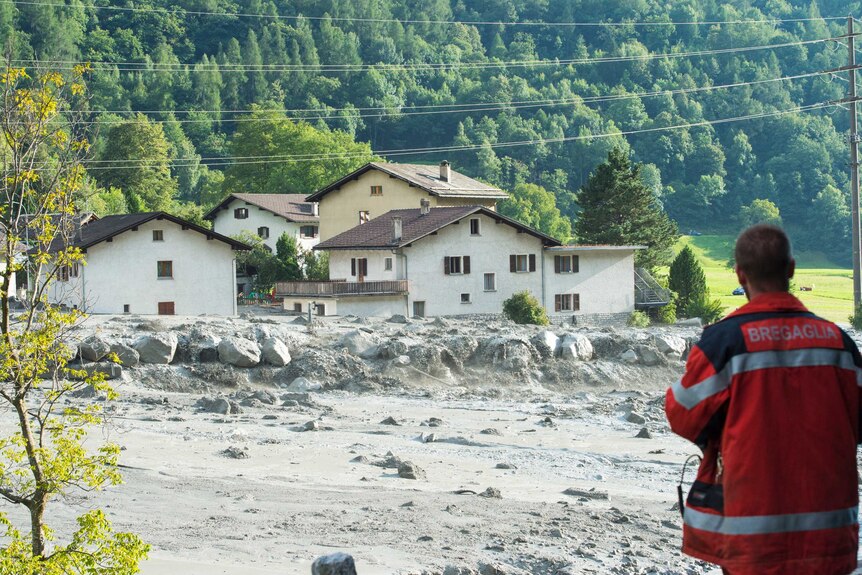 Mud rushes past homes in the Swiss village of Bondo. The houses seem undamaged.