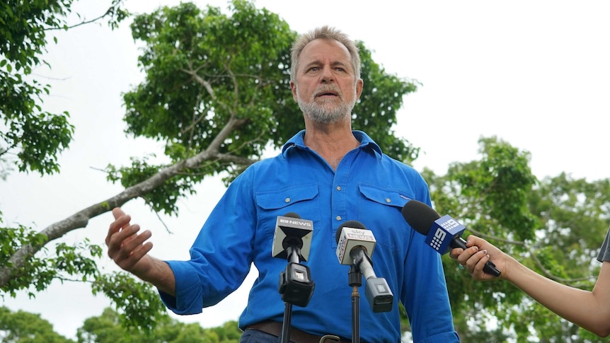 Nigel Scullion stands in front of microphones as he addresses the press