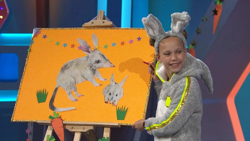 Whyla dressed as a bilby next to a board with a picture of a bilby