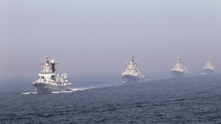 Four Chinese missile destroyers are seen sailing in line across the ocean.