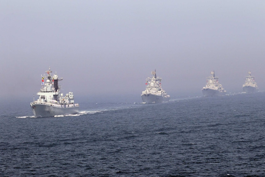 Four Chinese missile destroyers are seen sailing in line across the ocean.