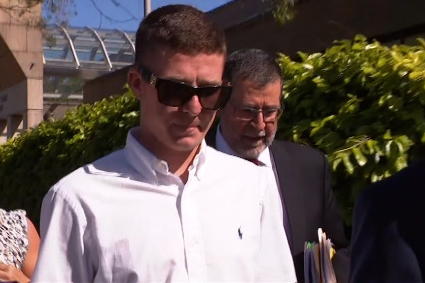 A man in sunglasses flanked with his lawyers walks outside of court