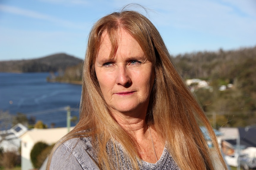 woman with red hair looks into sun with sea behind her