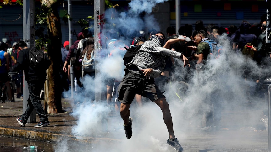 A protester throws back a tear gas canister at police amid smoke.
