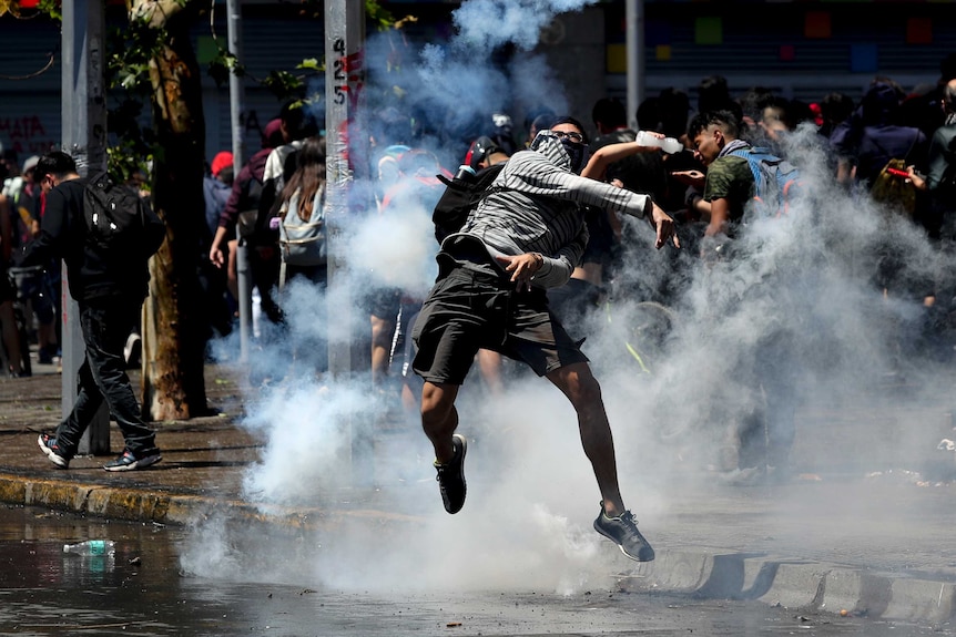 A protester throws back a tear gas canister at police amid smoke.