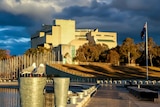 The High Court on the shores of Lake Burley Griffin. There are dark clouds over the building, and a seagull in the foreground.