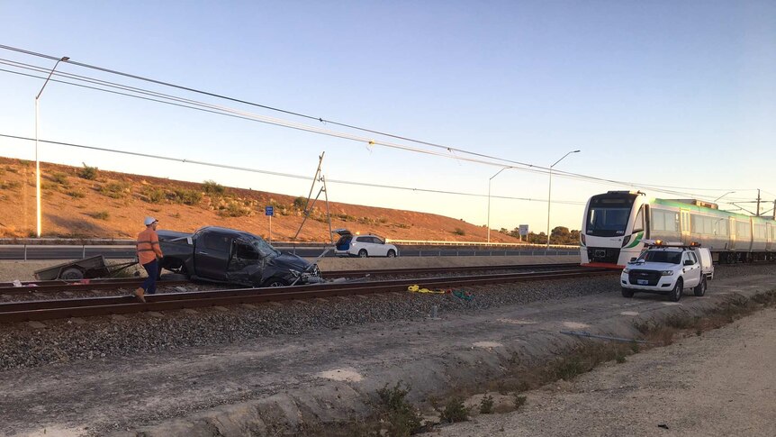 The car lies across the tracks, a rail worker stands nearby and a train sits about 50 metres away.
