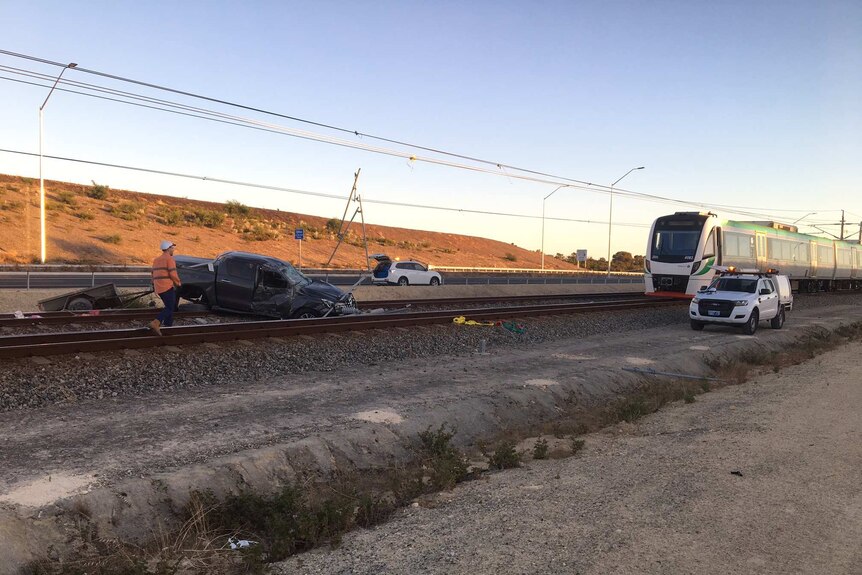 The car lies across the tracks, a rail worker stands nearby and a train sits about 50 metres away.