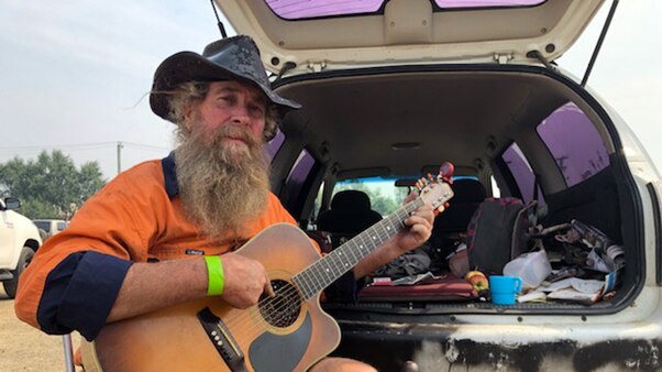 Paul Joseph strums a guitar at an evacuation story