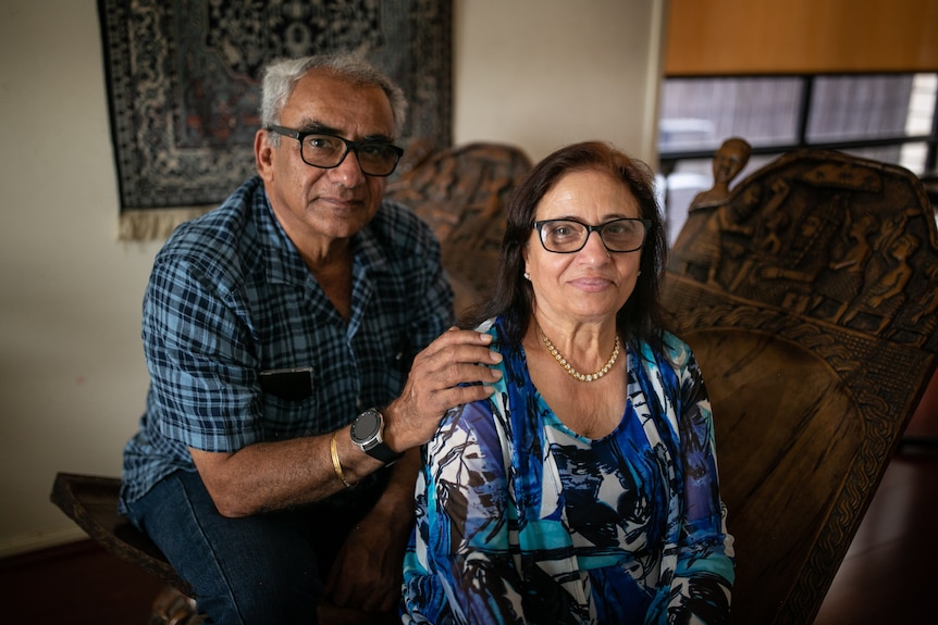 A older Indian man and woman. He has his hands on her shoulders.