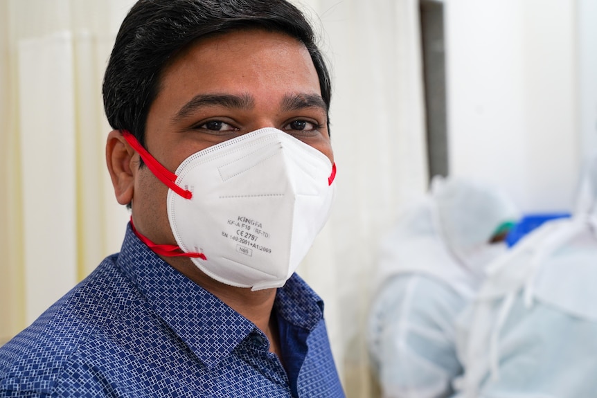 An Indian man in a blue shirt and a white face mask