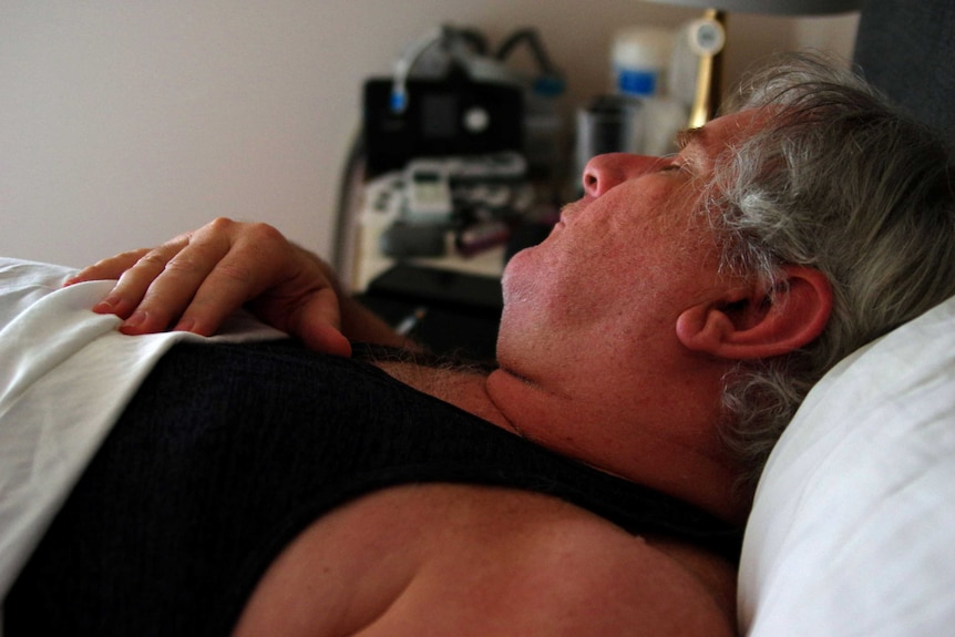 A side-on shot of a man with grey hair lying down on his back with a hand on his chest.