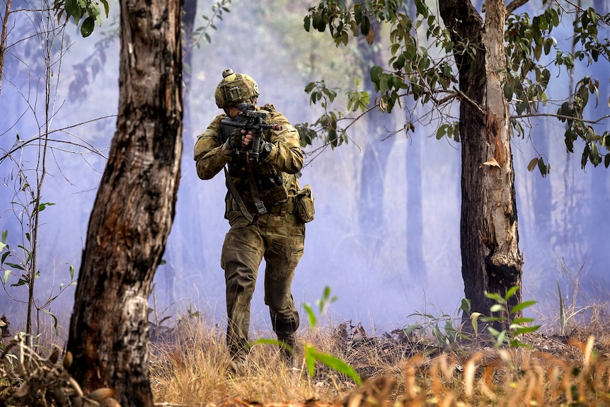 Armed Australian soldier looks through the sights of his machine gun, as he walks through bush